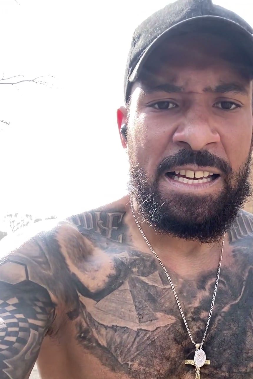 Eddie, shirtless outdoors in a cap, his chest piece and cross showing