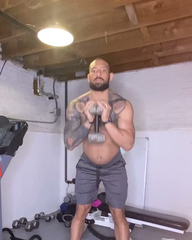 Eddie holding a dumbbell at his chest in his home gym