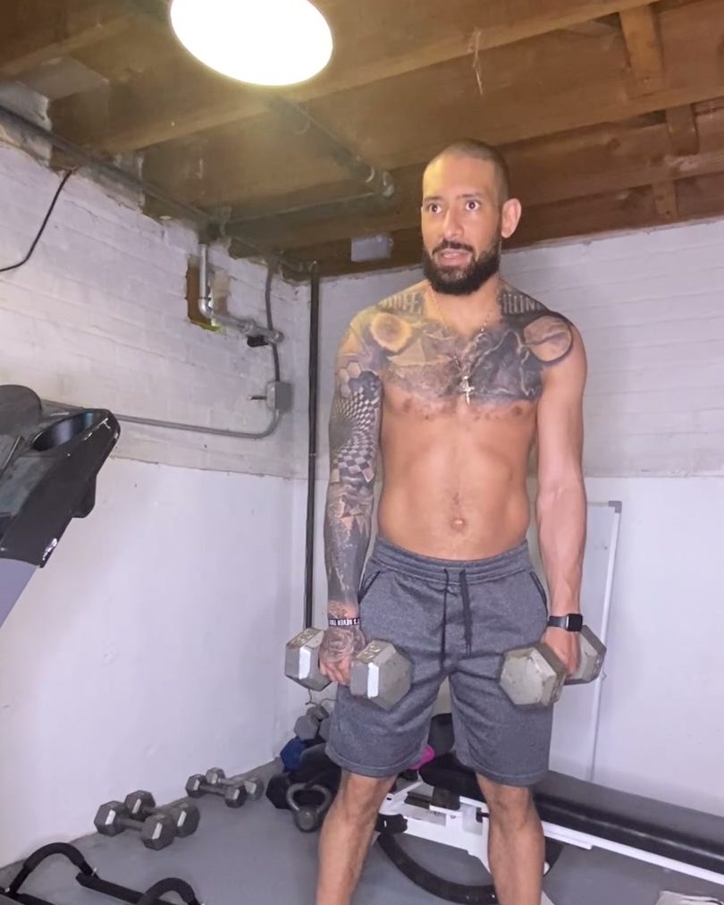 Eddie holding two dumbbells at his sides in his home gym